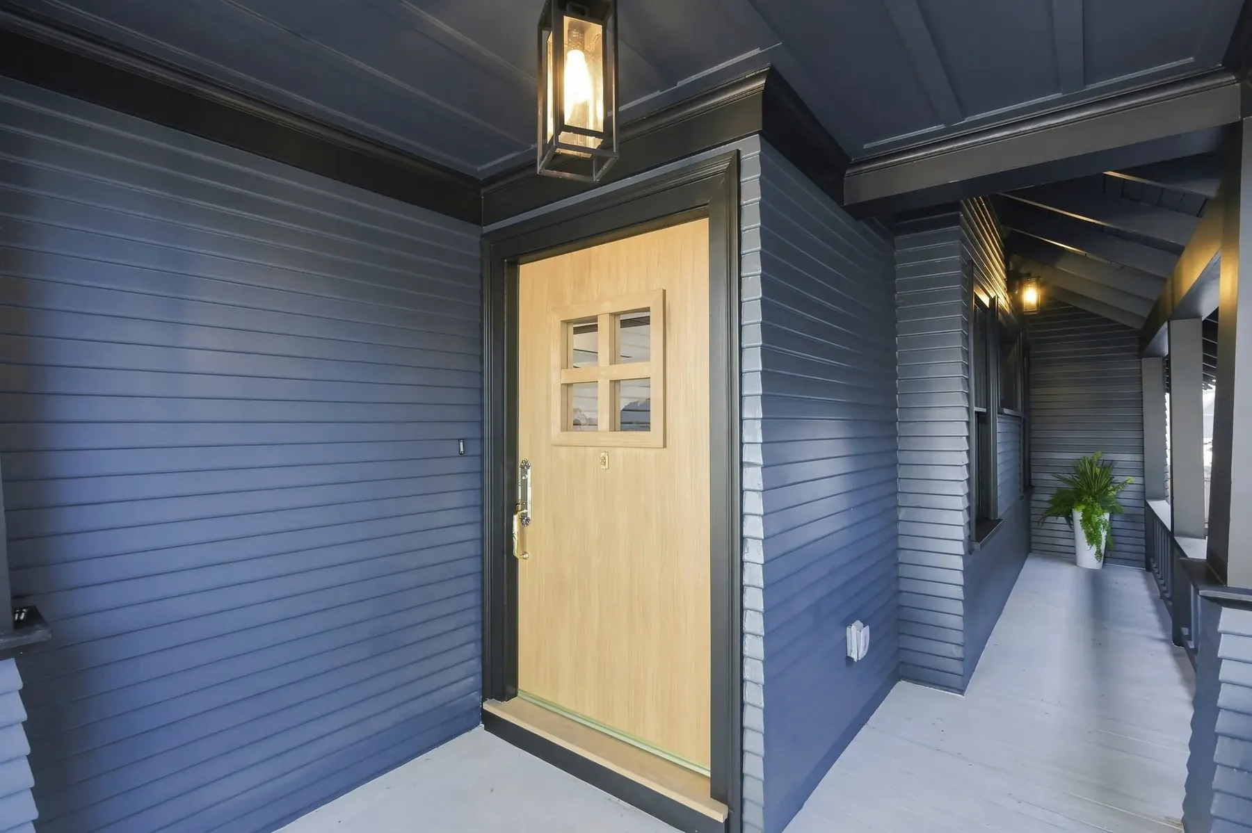 The entry looking in. A new white-oak door against the blue siding, with the original covered porch depth kept intact.