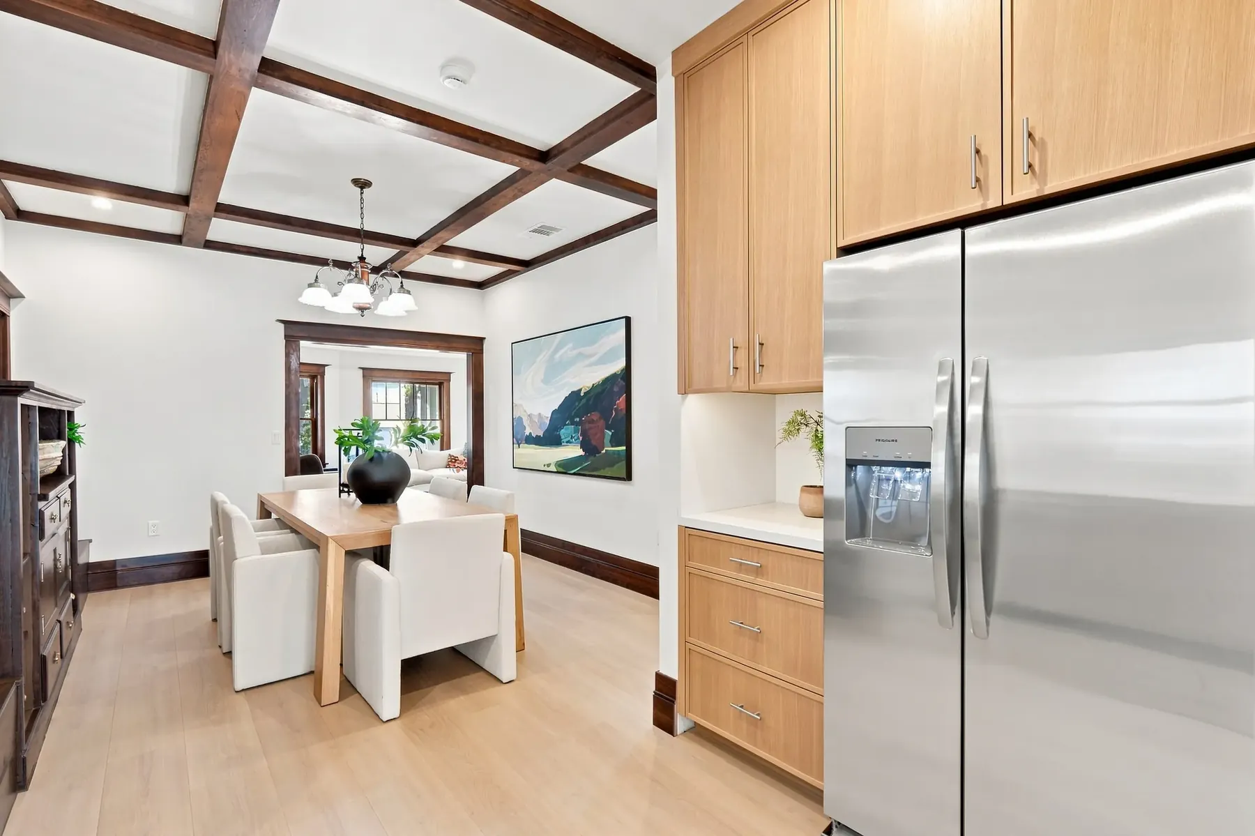 The open plan from the kitchen side. Sight line runs from the range through the dining room to the front windows.