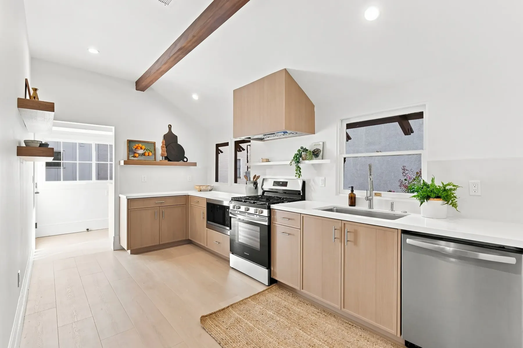 Full run of white-oak cabinetry with a quartz counter and integrated sink under the window.